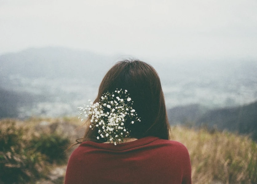 Woman with brown hair, red top and white flowers looks away from the camera towards the horizon with a calm feeling.